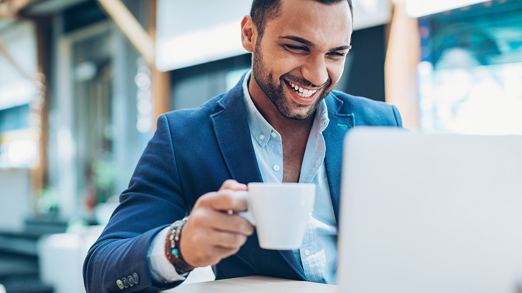 Smiling man on laptop with hot drink